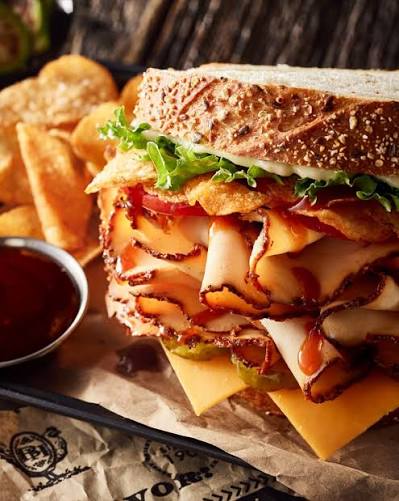 Deli sandwich stacked with turkey, cheese, and lettuce, served with chips